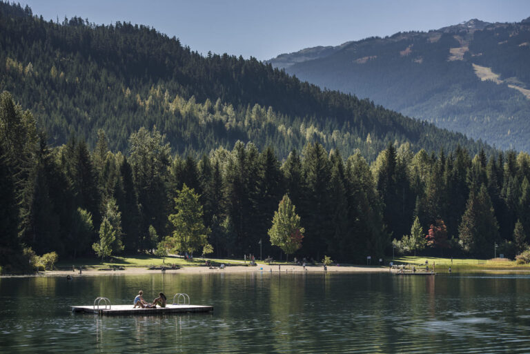 People relaxing on a floating dock at Lost Lake with scenic mountain and forest backdrop in Whistler